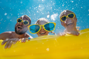 Alt image text: Three people on pool floatie in the sunshine.