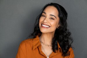 A woman in an orange blouse smiling with veneers